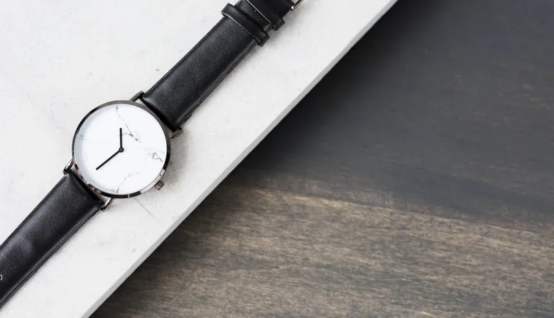 A minimalist white-dial watch on a black strap, laid on wood